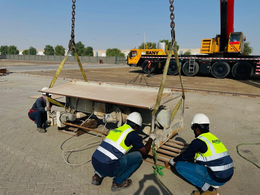 Aerolift crew in branded hi-vis vests rigging a crane end carriage with slings and chains beneath a mobile crane hook