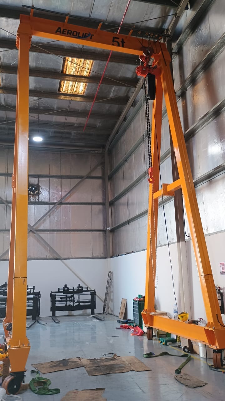 Aerolift-branded portable gantry crane marked 5 t with a chain hoist and hook, standing inside a steel-framed workshop bay